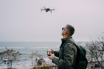  A man driving a drone with a remote control against the backdrop of the sea in foggy weather....