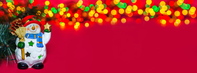 Holiday greeting banner. Toy Christmas snowman with star on red background. Composition of Christmas tree, berries, Apple and colorful bokeh lights garland. Classic atmosphere of new year. Copy space