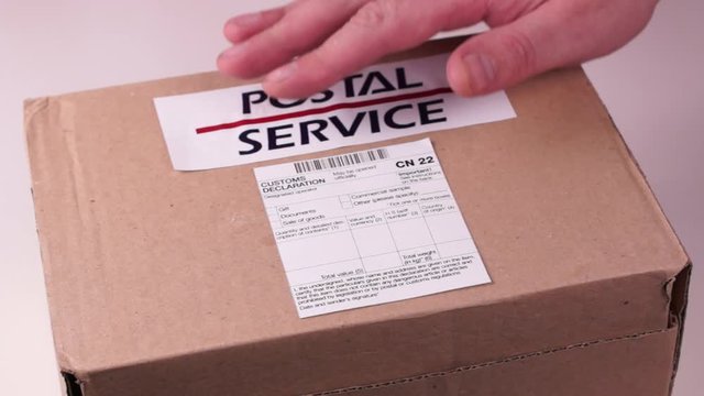 Human sticks a Customs declaration form CN22 on a Parcel with a label postal service on a white background. Close-up