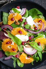 Detox salad with tangerines, mozzarella, herbs, pomegranate seeds and nuts on a dark background.