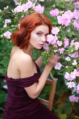 beautiful red-haired girl in arranger where azalea blooms in a colorful flying dress