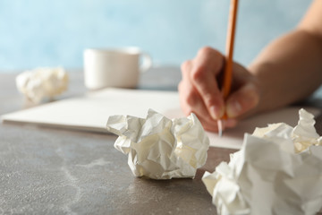 Person writes on grey table with paper balls and cup of coffee, close up