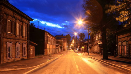 Street with classic wooden houses on both sides of the road at night in Irkutsk, Russia.