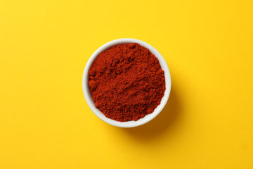 Bowl with red pepper powder on yellow, top view
