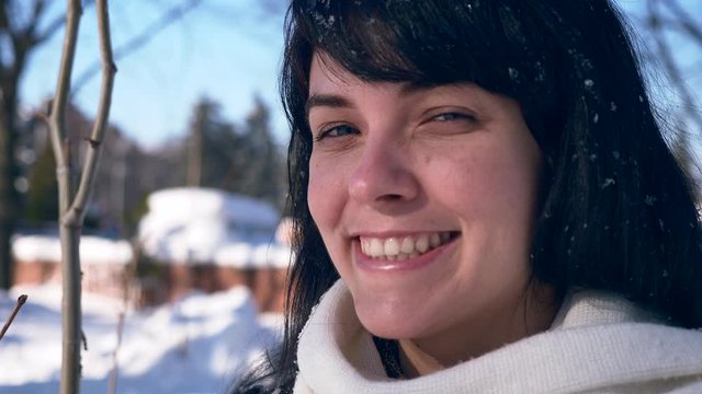 Close-up Pretty Female Face. Snowflakes On Hair. Young Adult In Snow Covered City Park On Sunny Day. Slow Motion 30 fps 0.5 normal speed 60 fps