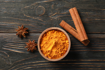 Wood bowl with turmeric and cinnamon on wooden background, top view