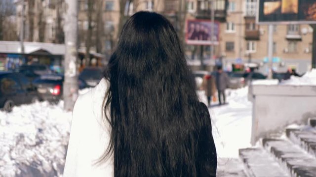 Camera Follows Brunette Female Walking Down The Street. Winter City Life. Slow Motion 30 fps 0.5 normal speed 60 fps
