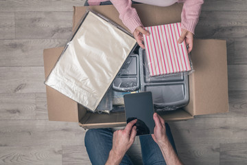 Couple man and woman shopper using tablet checking order sitting on floor at home and opening...