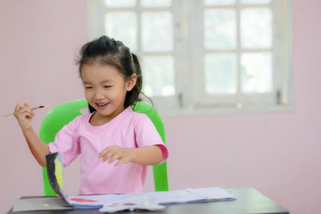 Naklejka premium An Asian kindergarten girl is coloring on the table.