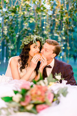 Close up of funny happy wedding couple eating burger, sitting in stylish rustic reaturant outdoors