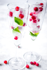 ice cubes with red berries and mint in glasses on white background