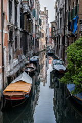 Fototapeta na wymiar Narrow canal between old houses, boats on dark water. Arch bridge. Venice, Italy.