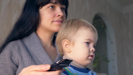 Pretty Mother With Remote Control in Hand and Cute Child Watching Personal Home Video. Sitting On Sofa Couch In Room. Slow Motion 30p 0.5 Real Time Speed