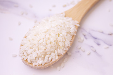  rice wooden spoon on white marble background. close-up, sprinkled rice
