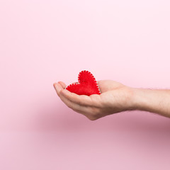 Male hand holding a handmade heart on a pink background. Valentine's day concept, symbol of love, print commercial blank, copy space.