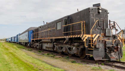Fototapeta na wymiar Old diesel locomotive with trains cars in a field.