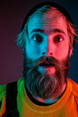 Shocked, astonished, close up. Caucasian man's portrait on gradient studio background in neon light. Beautiful male model with hipster style. Concept of human emotions, facial expression, sales, ad.