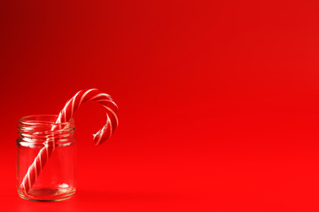 One Lollipop Candy cane in a glass jar on a red background.