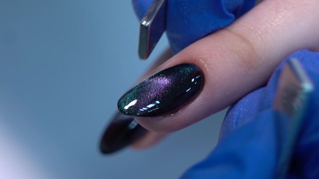 Closeup view of hands of professional manicurist doing modern trendy holiday naildesign using magnets and special glossy sparkling gel polish with shiny cats eye effect. Full hd video footage.