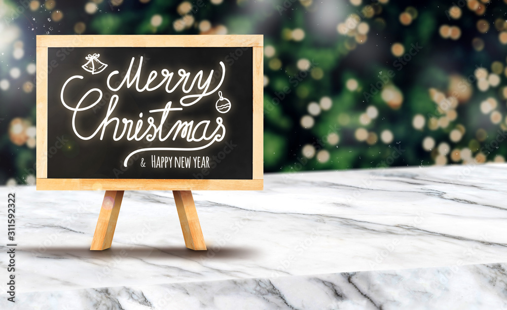Poster Merry Christmas on blackboard on white marble table at blur bokeh Christmas tree with string light background when snow falling,Winter holiday greeting card