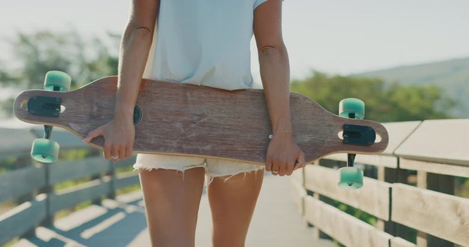 Tight shot of a skater girl holding her longboard skateboard walking in slow motion, surf skate culture concept