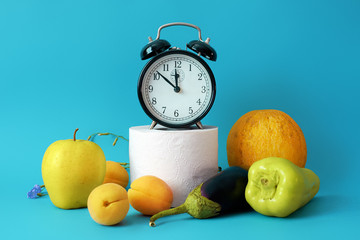 Alarm clock, fruits and toilet paper on a blue background. Natural remedy for constipation. The...