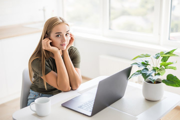 Young woman in kitchen using laptop. Happy woman looking at laptop while standing in kitchen in morning.