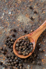Peppercorns in wooden spoon on texture background