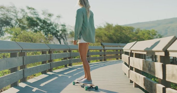 Attractive skater girl riding her skateboard on a coastal boardwalk in slow motion, looking back smiling at the camera