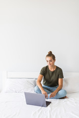Happy casual beautiful woman working on a laptop sitting on the bed