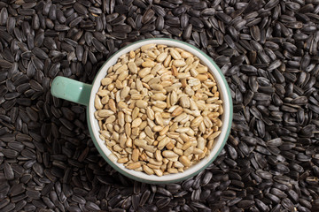 peeled sunflower seeds sprinkled in a small colored bowl on a background of unpeeled black sunflower seeds