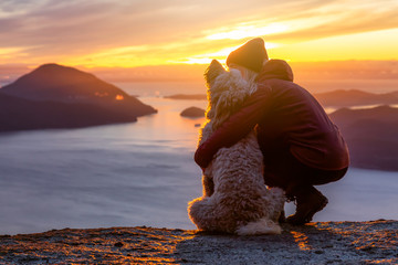 Adventurous Girl Hiking on top of a Mountain with a dog during a colorful sunset. Taken on Tunnel Bluffs Hike, near Vancouver and Squamish, British Columbia, Canada.
