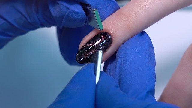 Closeup view of hands of professional manicurist doing modern trendy holiday naildesign using magnets and special glossy sparkling gel polish with shiny cats eye effect. Real time full hd video footag
