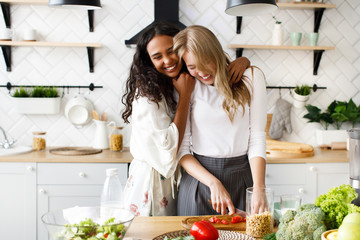 Two beautiful young girls are making a healthy breakfast and hugging near the table full of fresh...