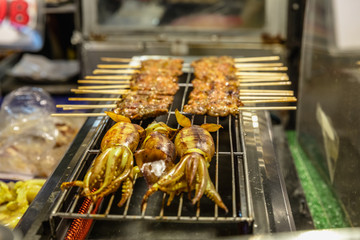 Squid and sate skewers on a grill at the Ratchada Night Market in Bangkok