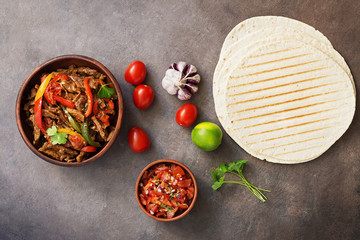 Mexican dish fajitas meat with vegetables and salsa sauce on a dark rustic background. Flat lay, overhead.
