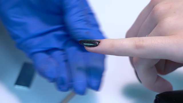 Closeup view of hands of professional manicurist doing modern trendy holiday naildesign using magnets and special glossy sparkling gel polish with shiny cats eye effect. Real time 4k video footage.