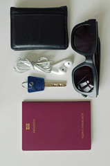 Flat lay travel items: European passport, sunglasses, wallet, earphones and a key.
