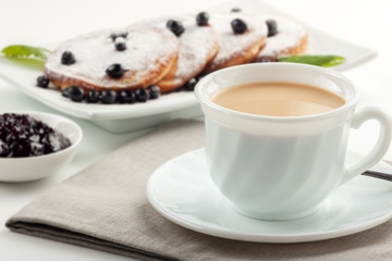 A Cup of coffee with milk and a plate with a pancakes is on the table.