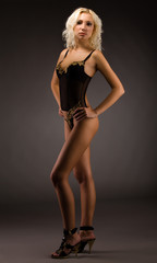 Fototapeta na wymiar Young woman in black lingerie standing over dark background
