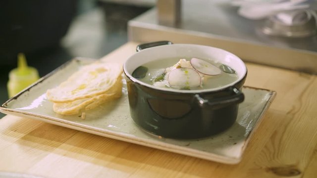 Close up handheld shot of chef male pouring olive oil on a white slice of bread, a plate with ukha and slice of white bread ready to serve in the restaurant.
