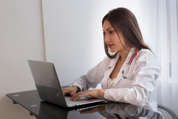 Joven medica en consultorio digitando y esperando paciente para consulta medica