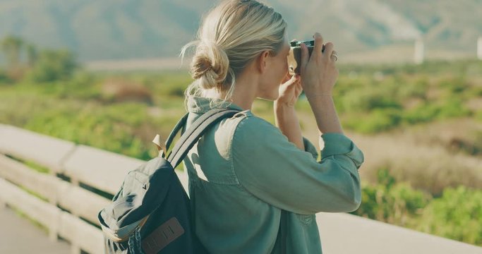 Young attractive woman smiling and laughing as she takes photos outdoors with a vintage camera, happy woman on her dream travel trip