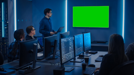 Team of Professional IT Developers Have a Meeting, Speaker Talks about About New Concepts, On Wall TV has Green Mock-up Screen. Concept: Software Development, Deep Learning, Artificial Intelligence