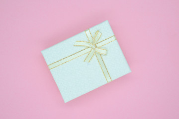 Light beige gift box with golden linen and a bow on a pink background