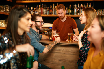 Group of friends drinking beer, chatting and having good time at pub. Night out.
