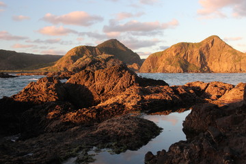 Sunset light over the mountains of Whatipu Beach in the Waitakere Ranges of Auckland, New Zealand.