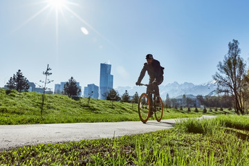 A cyclist rides on a road in the city against a background of green grass and mountains.