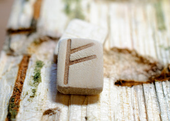 Wooden rune Fehu close-up on a wooden background. Soft focus