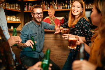 Group of friends drinking beer, chatting and having good time at pub. Night out.